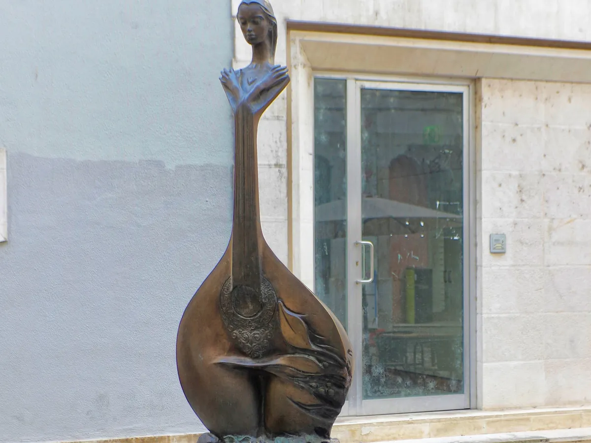 En bronzefigur formet som en portugisisk guitar står på brosten foran en lys mur