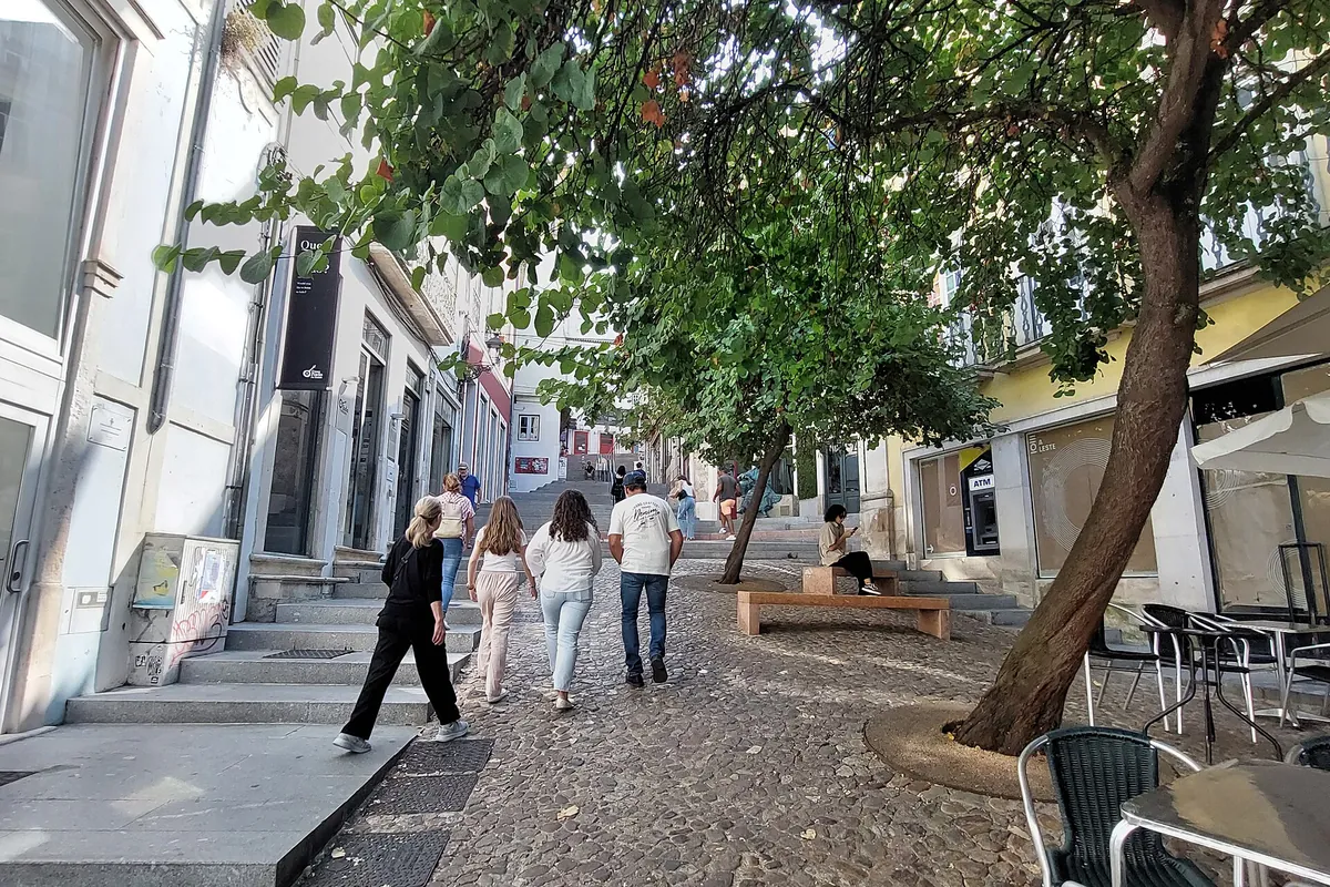 Rua de Quebra-Costas上一段鋪石街道，有枝葉扶疏的樹木、一段階梯，以及沿著淺色屋舍之間拾級而上的遊客